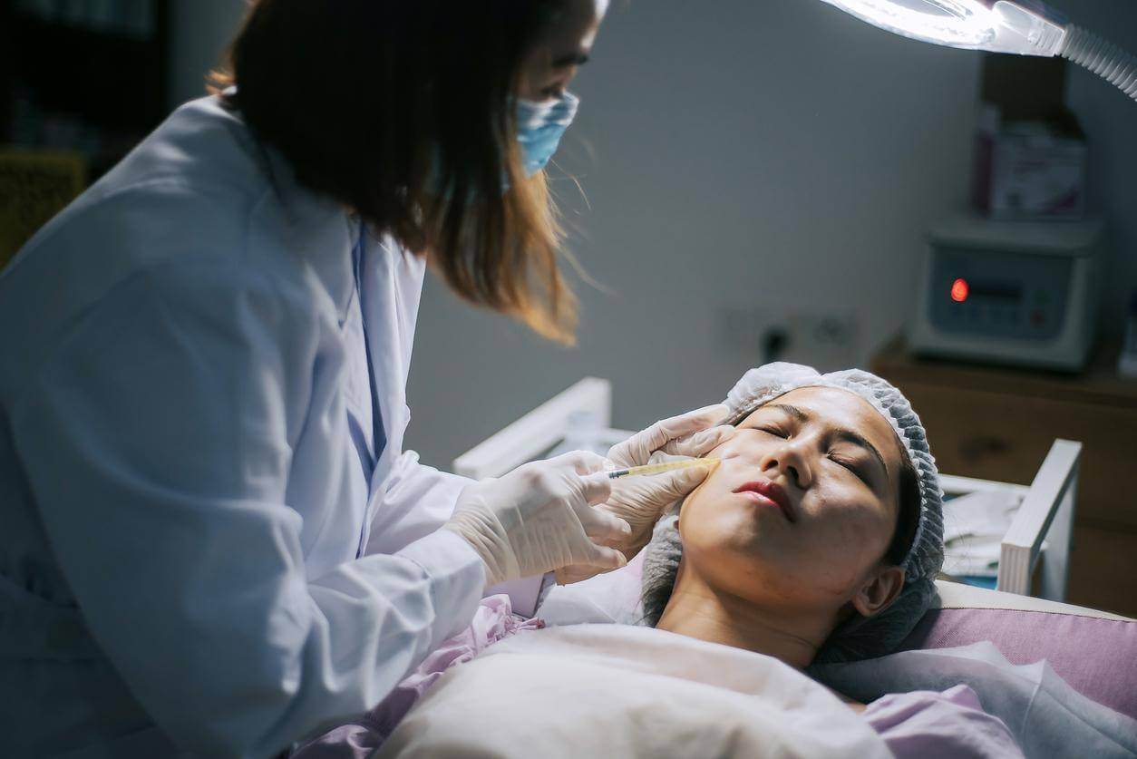 A woman getting a Botox treatment from a female professional at a beauty office.